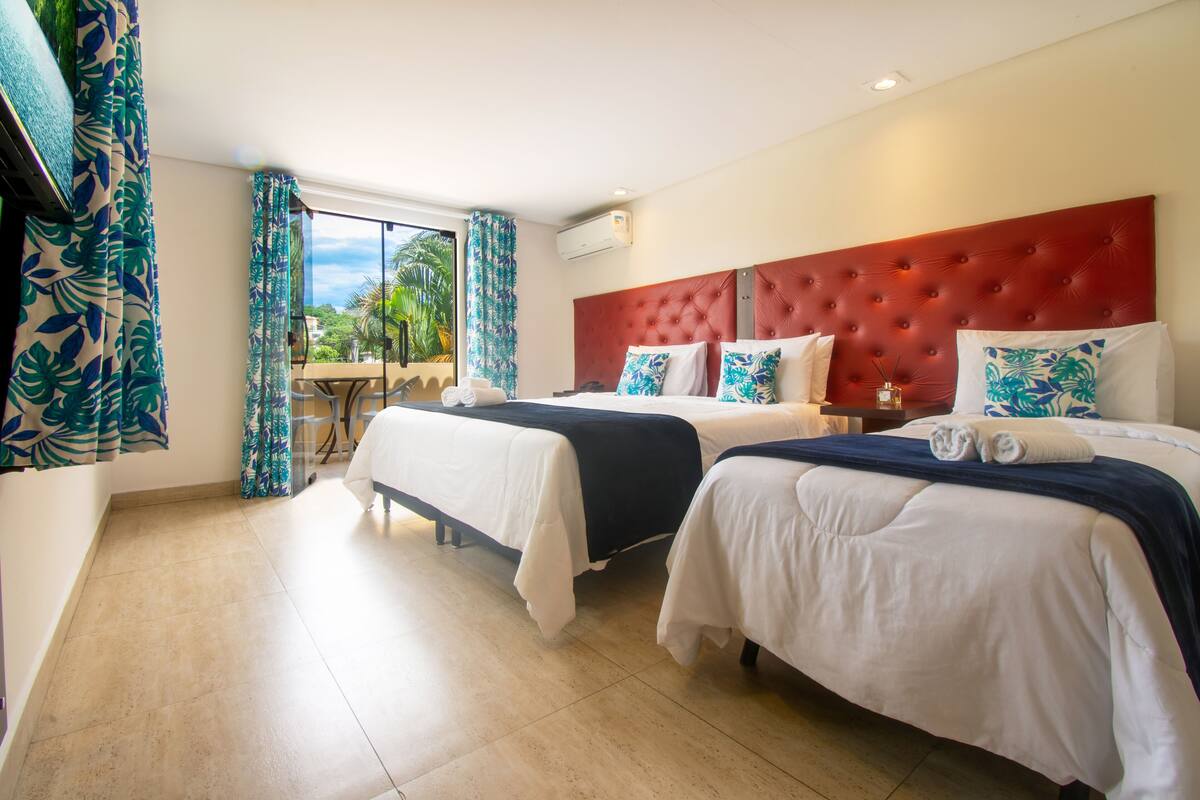 Une chambre d’hôtel avec deux lits, une tête de lit rouge et une vue sur l’extérieur.