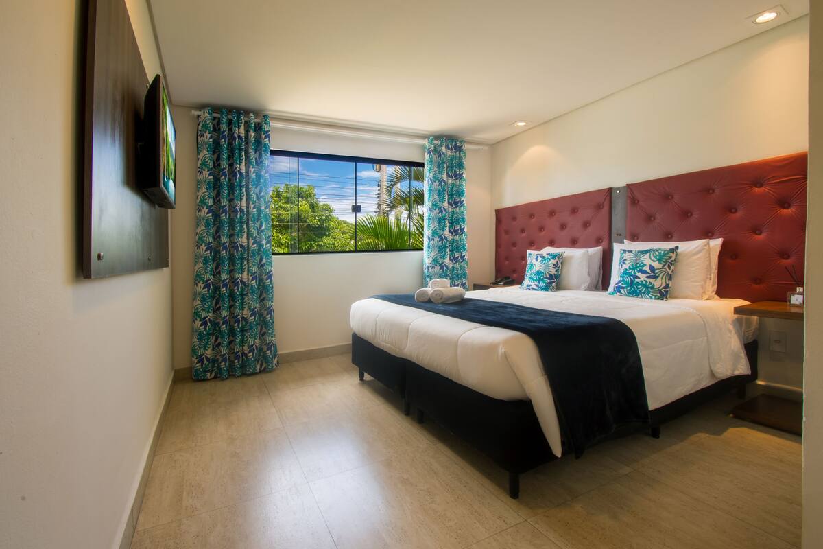 Une chambre d’hôtel moderne dotée d’un grand lit, d’un téléviseur à écran plat fixé au mur et d’une fenêtre avec des rideaux.
