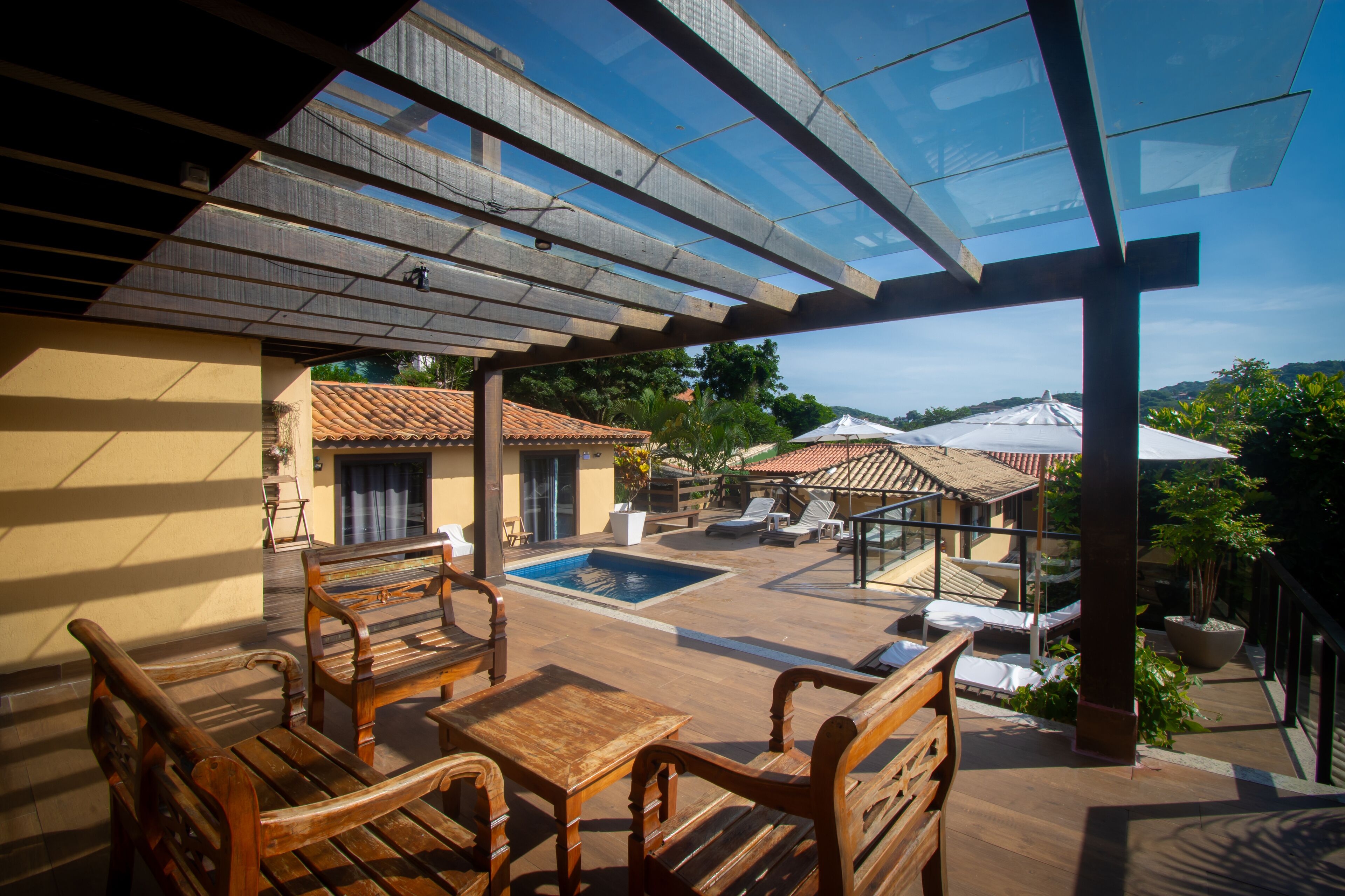 A covered outdoor area with wooden furniture, a swimming pool, and a view of the surrounding landscape.