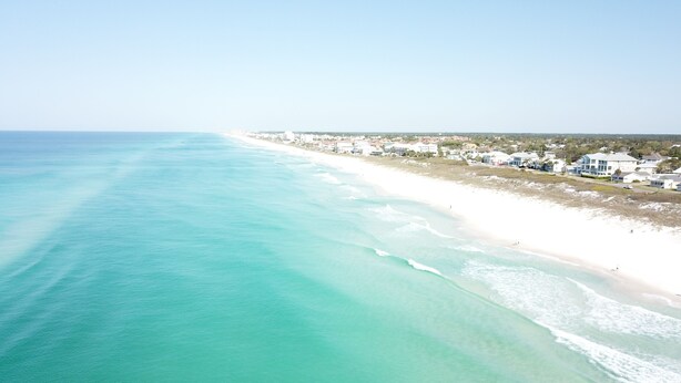 A coastal beach with clear turquoise waters and a row of white buildings along the shore.