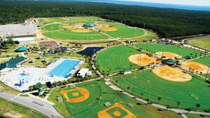 An aerial view of a sports complex with multiple baseball fields, a swimming pool, and a tennis court.