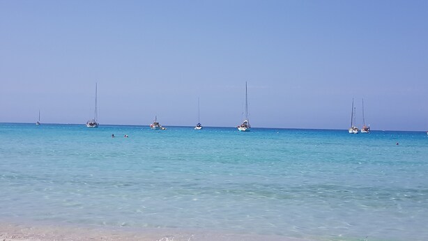A beach with clear turquoise water and several sailboats anchored in the distance. - Le Paradis à la Plage (Linguizzetta)