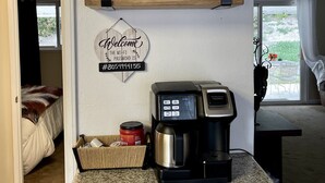 A kitchen with a coffee maker, a jar of lemons, and red mugs on shelves.