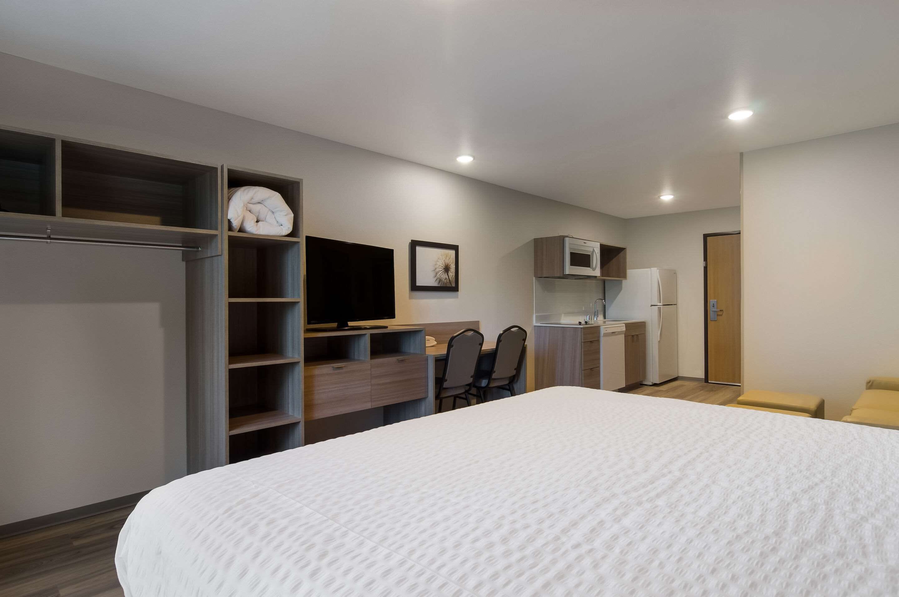 A modern hotel room with a large bed, a desk with a chair, a television, a microwave, and a wardrobe.
