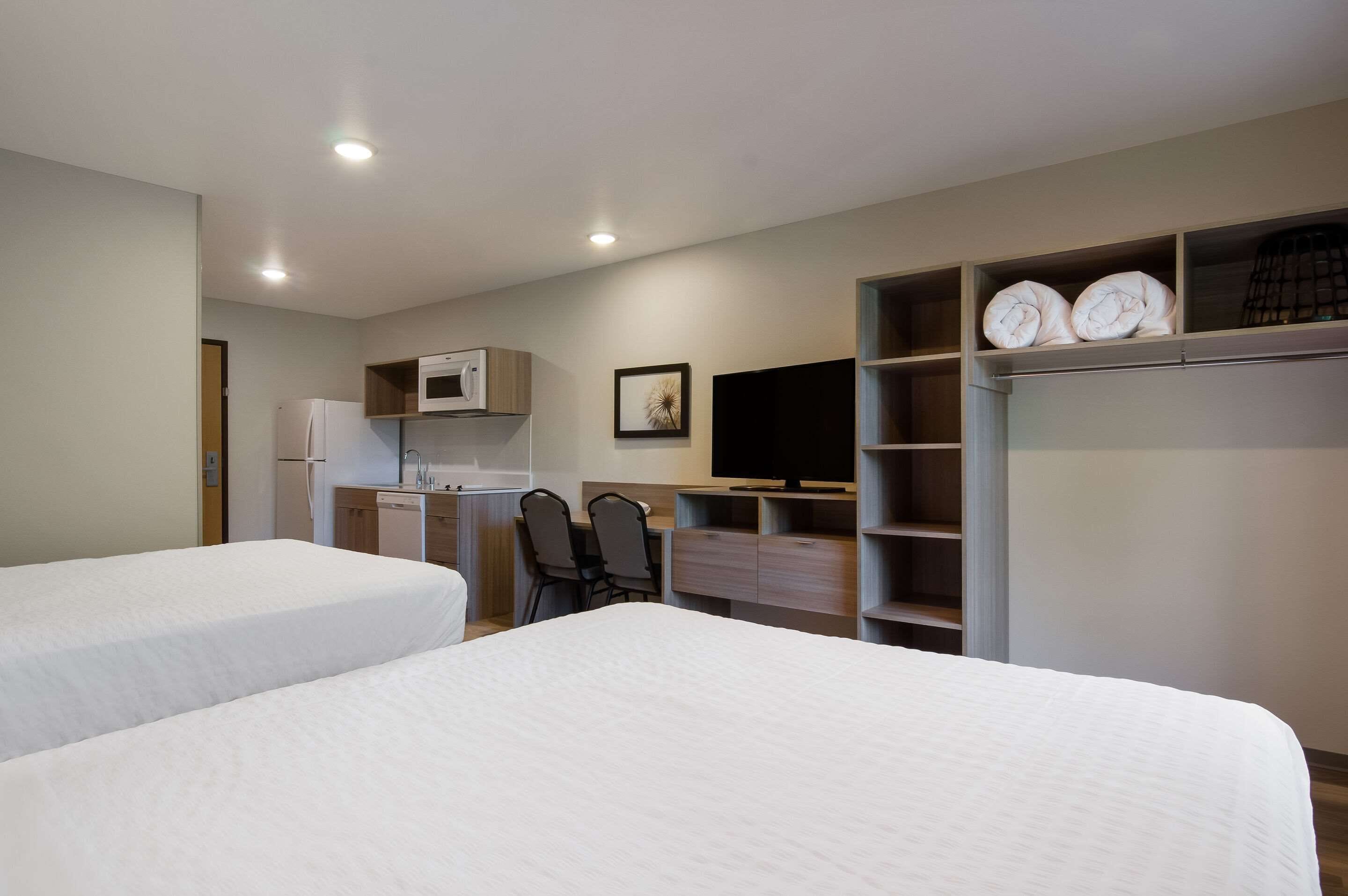 A hotel room with two beds, a desk with a chair, a microwave, a television, and a wardrobe with shelves.