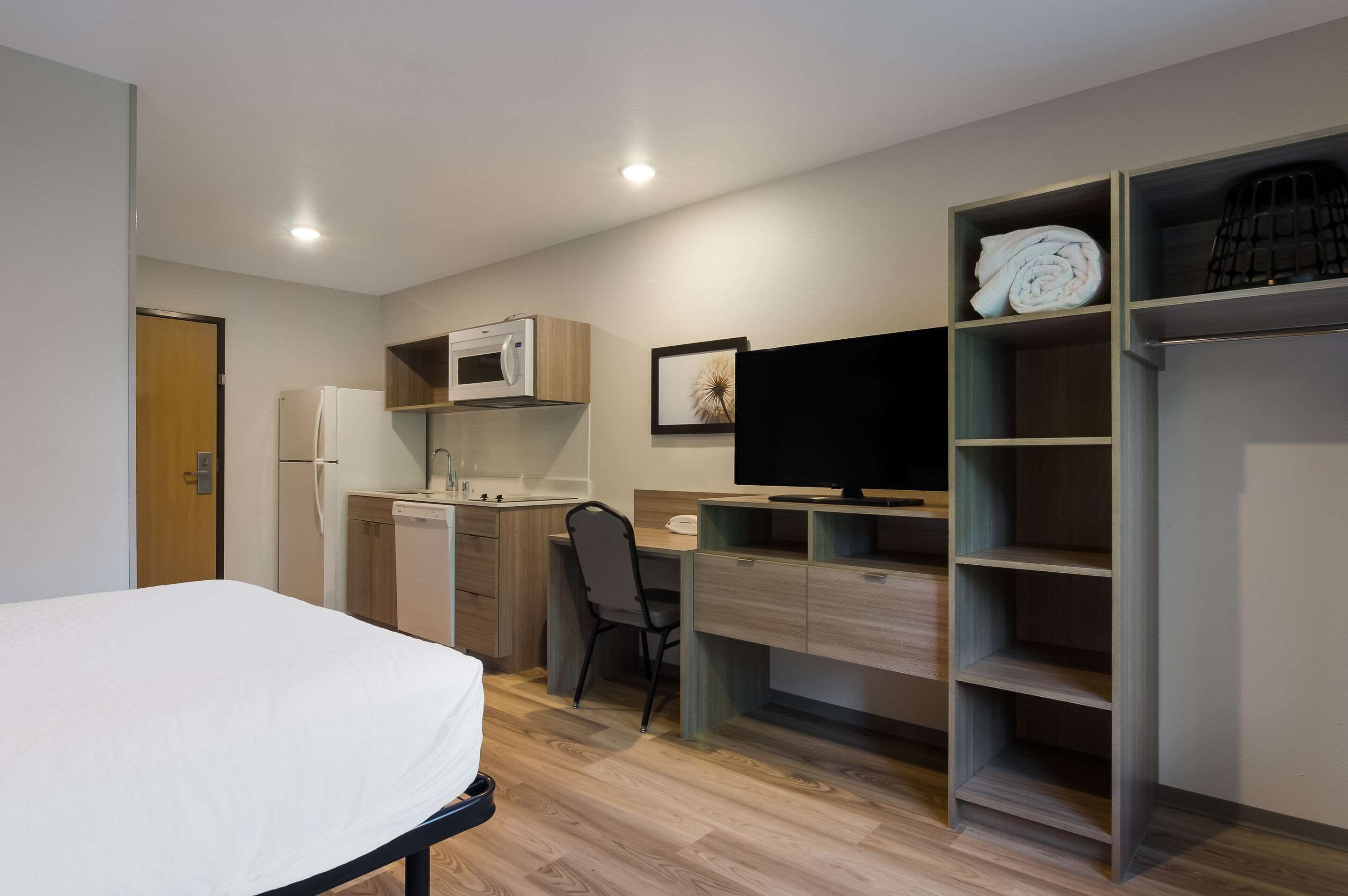 A compact room with a bed, a desk, a chair, a microwave, a refrigerator, a television, and a wardrobe.