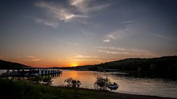 A sunset over a river with a dock and boats, surrounded by hills.