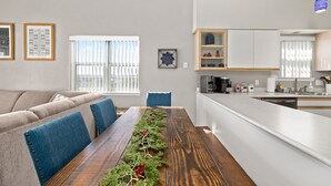 Een moderne woonkamer met een houten eettafel, blauwe fauteuils en uitzicht op de stad door grote ramen.