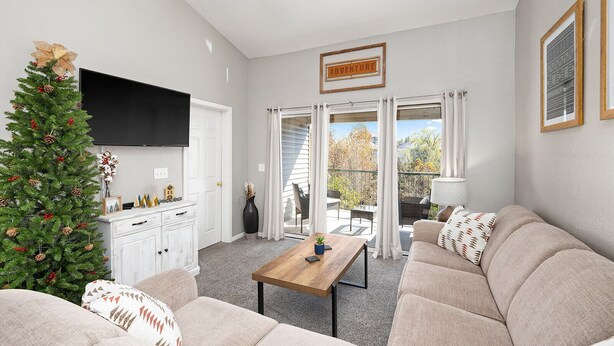 Een woonkamer met een kerstboom, een flatscreen televisie, een zithoek, een salontafel en een glazen schuifdeur naar een balkon.