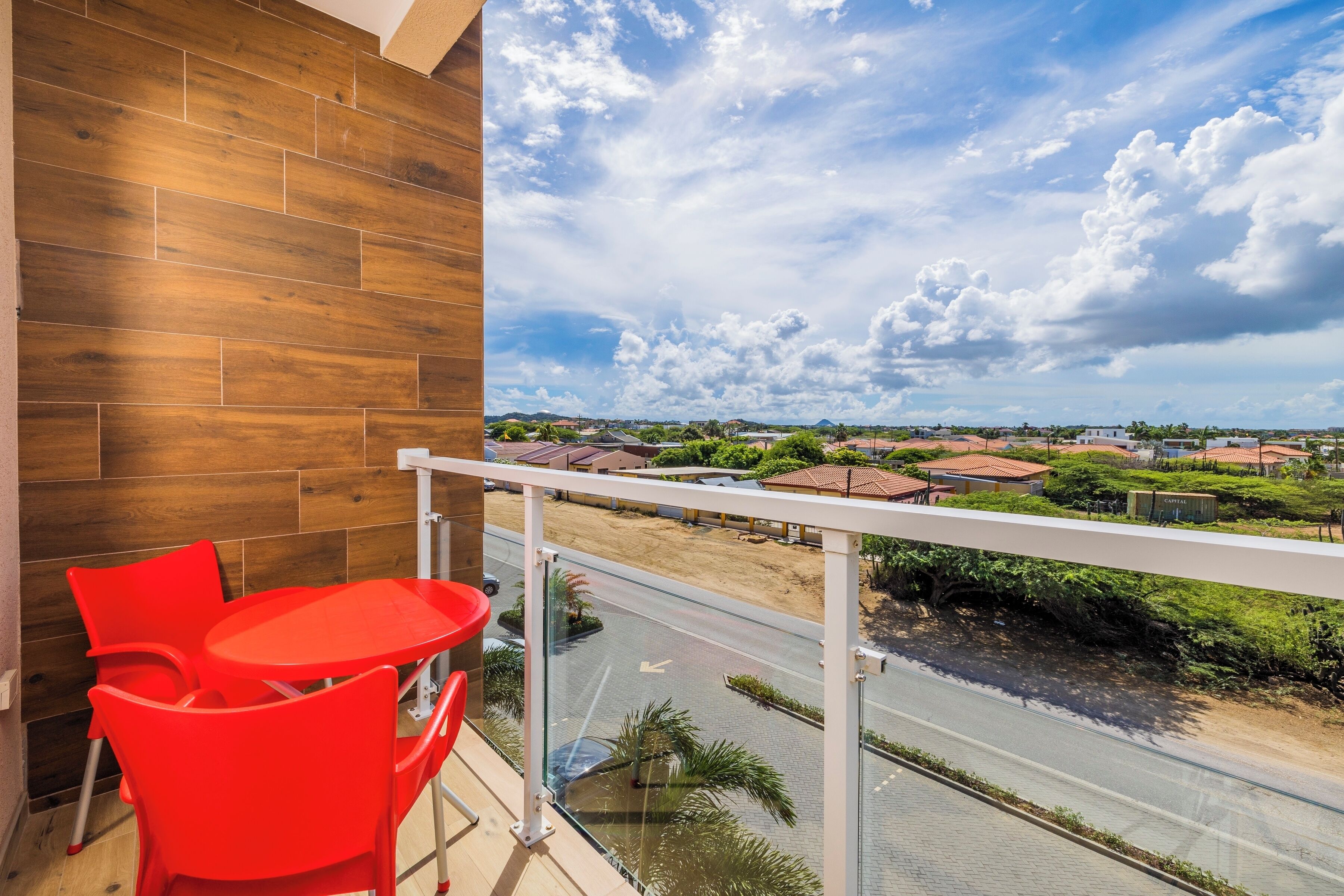 A balcony with a view of a residential area, a table with chairs, and a wooden wall.