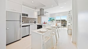 Una cocina moderna con electrodomésticos de acero inoxidable, un comedor con sillas blancas y vistas a la ciudad a través de amplios ventanales.