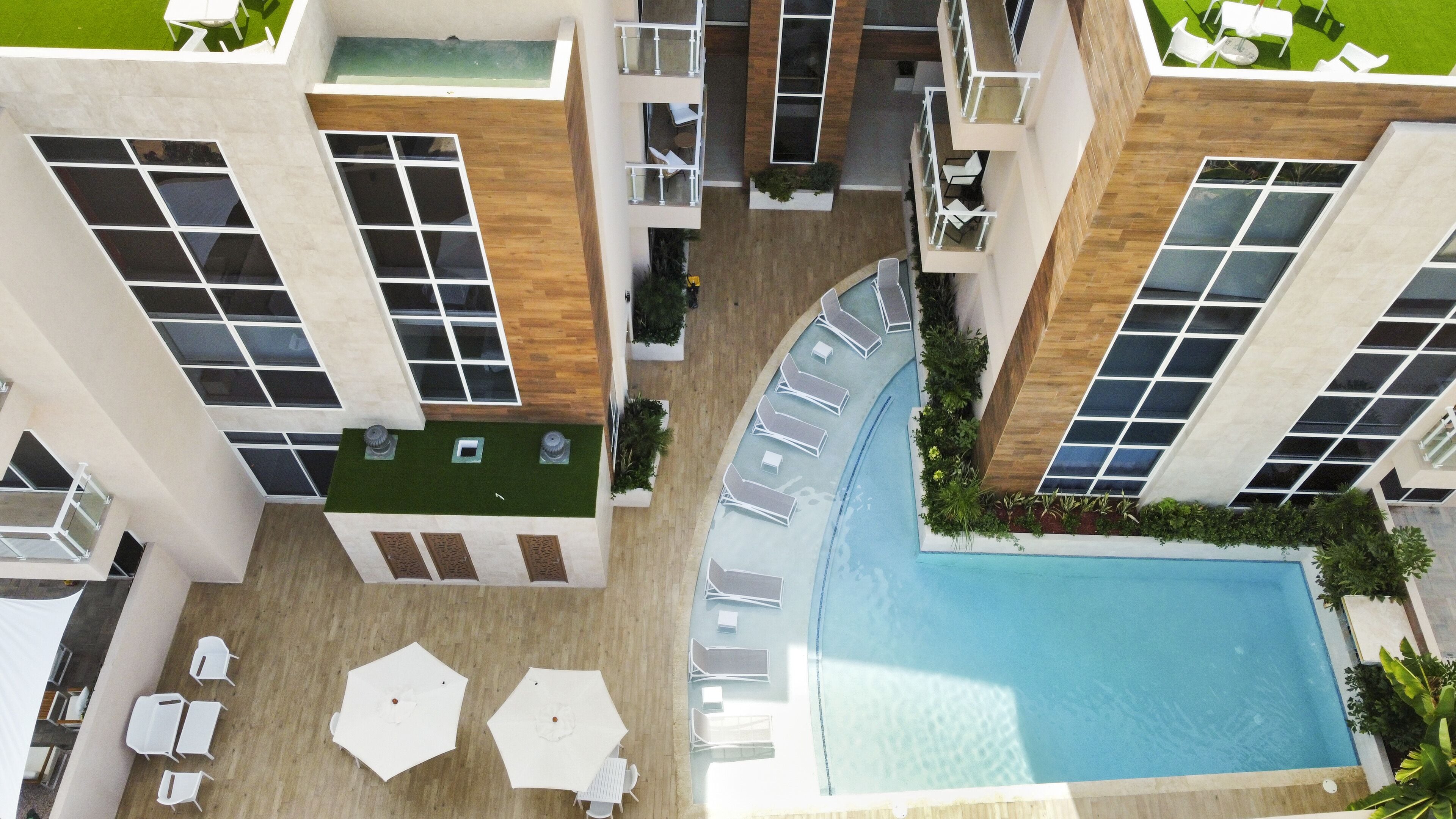 A modern hotel with a rooftop pool, outdoor seating, and a landscaped garden area.