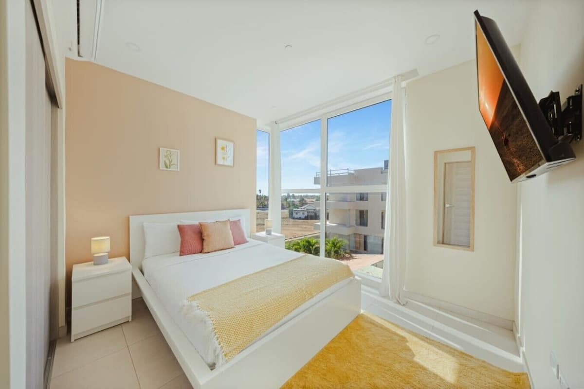 A bedroom with a bed, nightstand, and a window with a view of buildings.