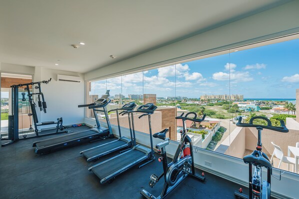 A gym with treadmills, stationary bikes, and weight machines, overlooking a cityscape.