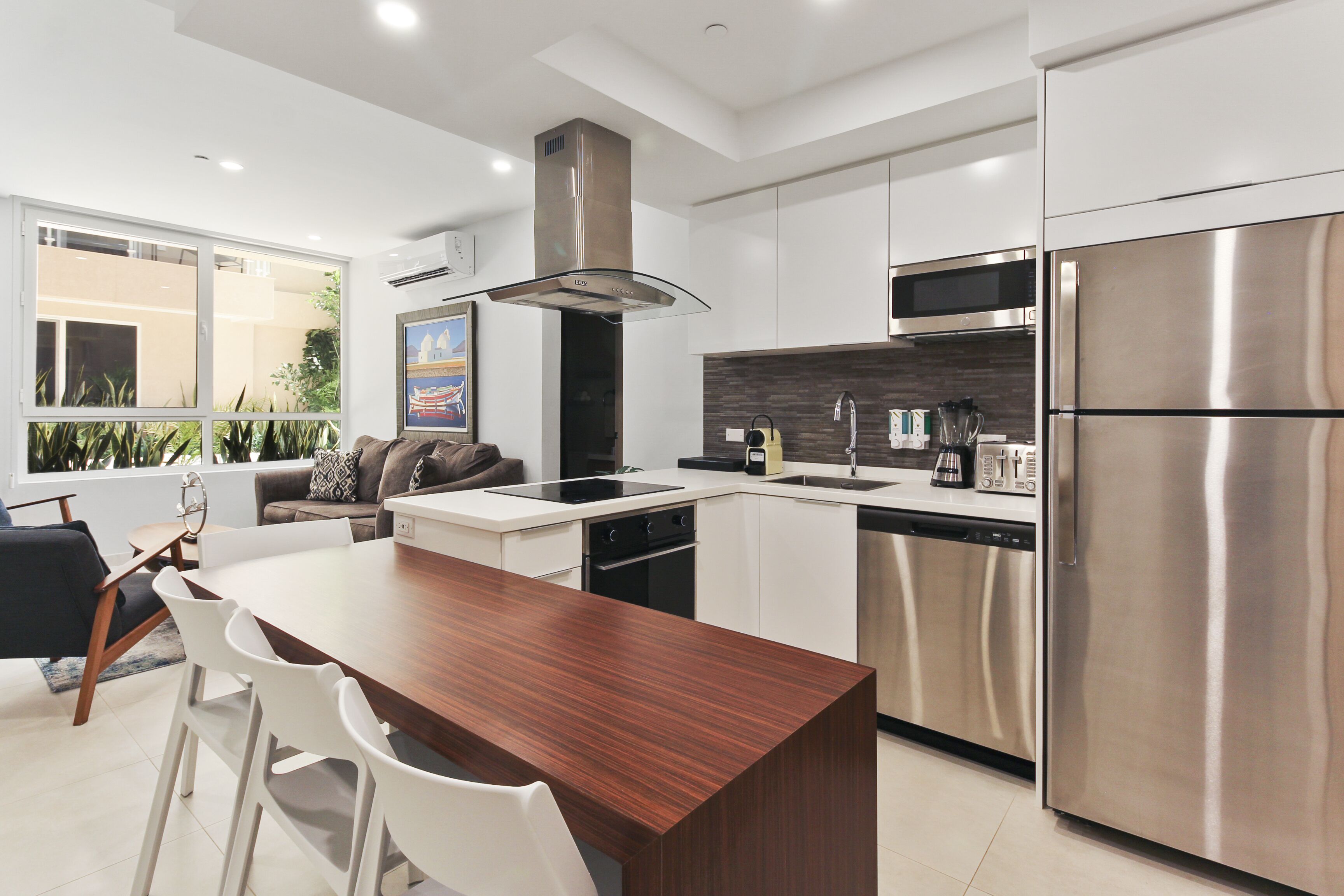A modern kitchen with a central island, stainless steel appliances, and a view of the outdoors.