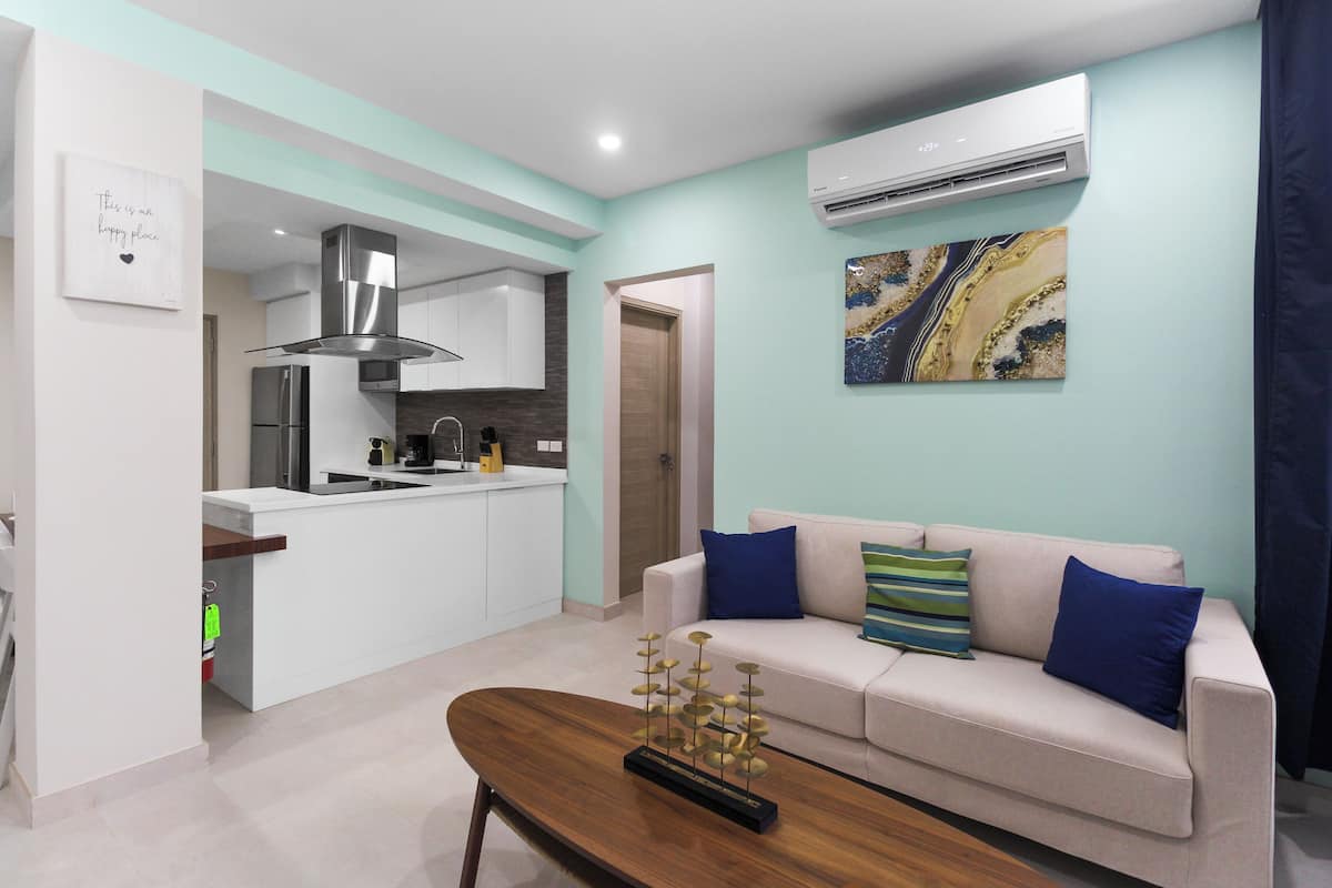 A modern kitchen with white cabinets, a stainless steel range hood, and a dining area with a wooden table and a decorative metal sculpture.