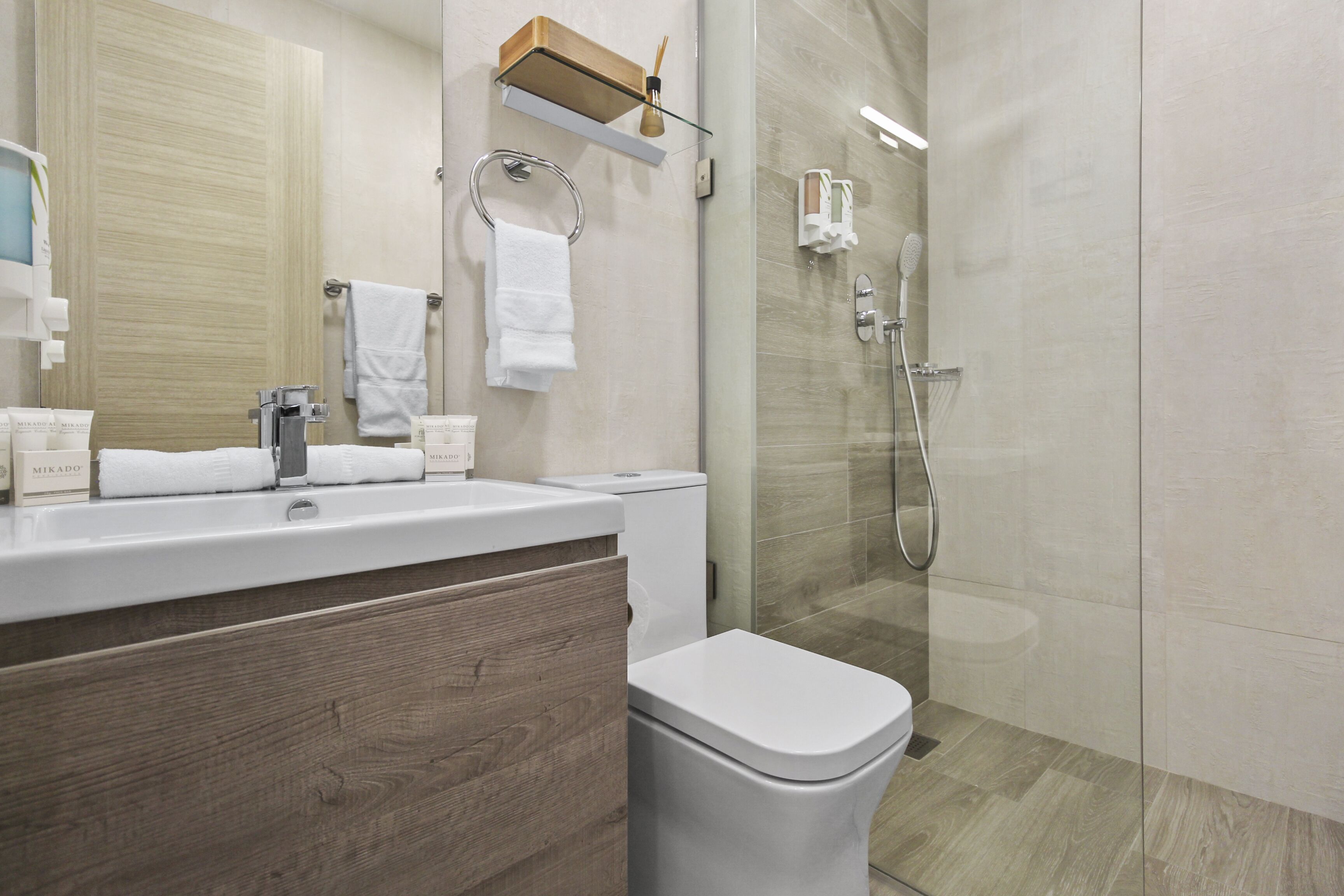 A modern bathroom with a wooden vanity, a toilet, a glass shower enclosure, and a towel rack.