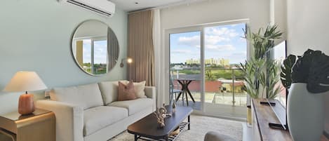 A modern living room with a sofa, coffee table, and chairs, a large mirror, and a view of a cityscape through a sliding glass door.