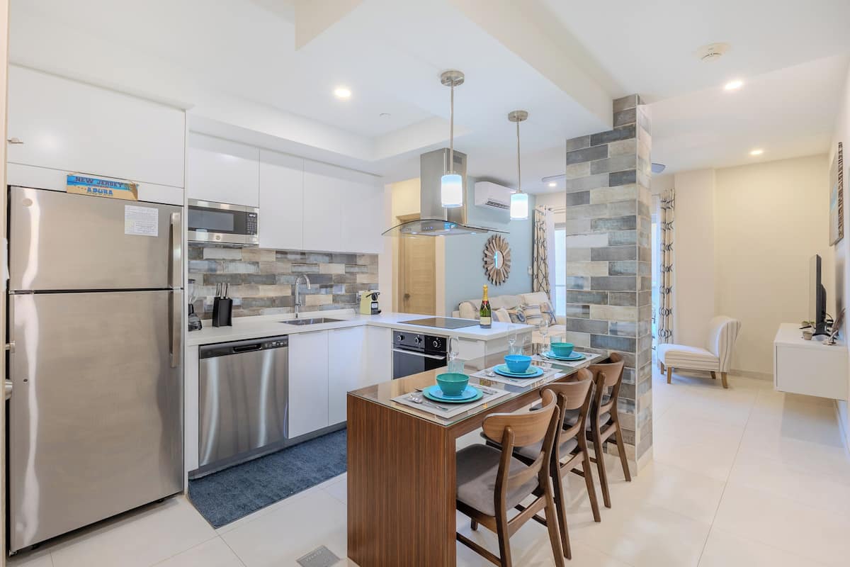 A modern kitchen with stainless steel appliances, a central island with chairs, and a dining area.