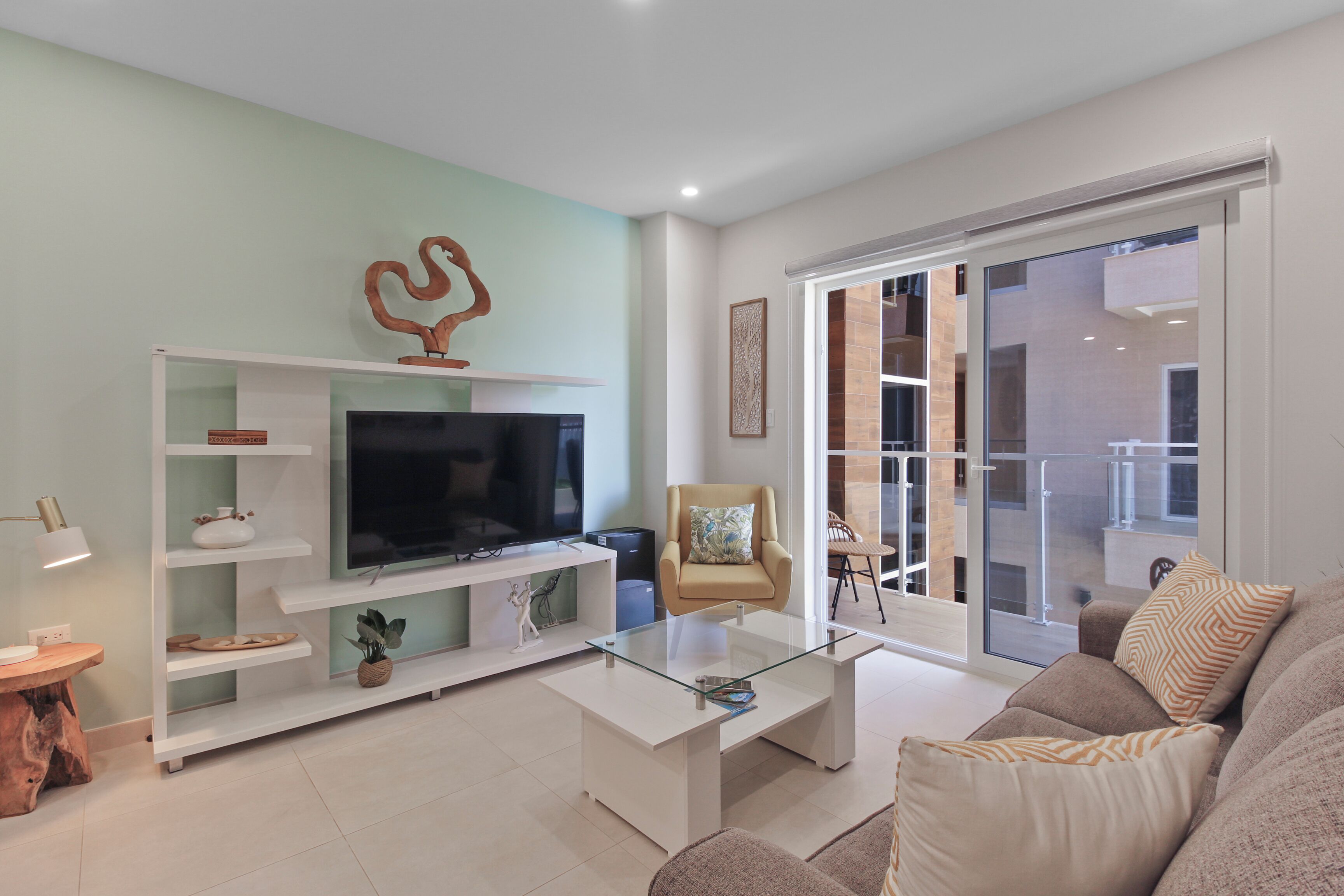 A modern living room with a flat-screen TV, a glass coffee table, a sofa, and a chair.