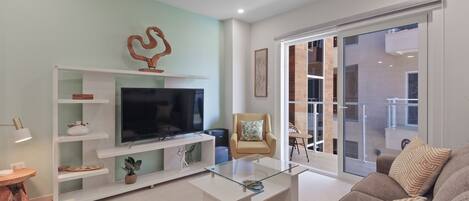 A modern living room with a flat-screen TV, a glass coffee table, a sofa, and a chair.