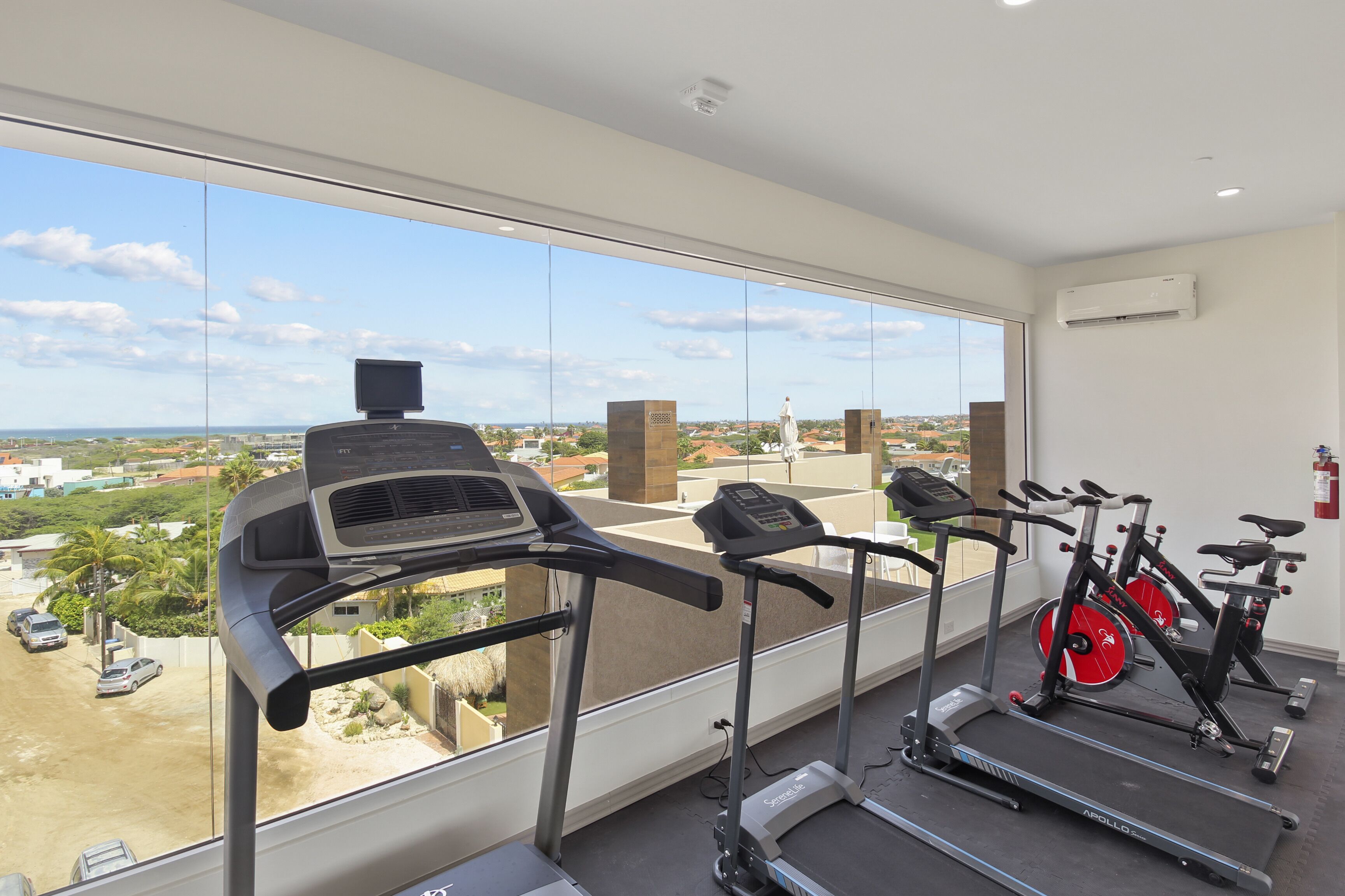 A gym with treadmills, stationary bikes, and a large window with a city view.