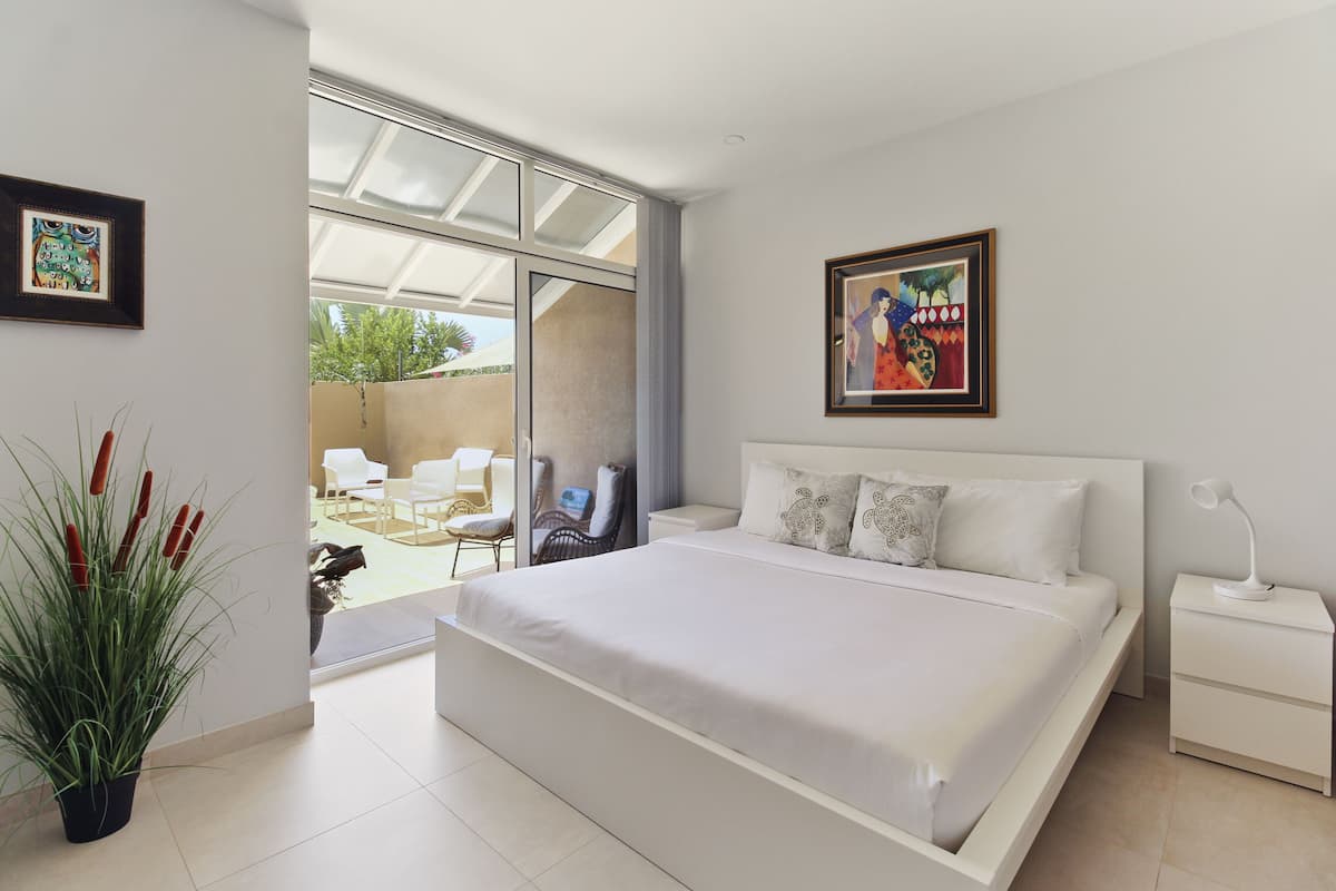 A modern bedroom with a large bed, a nightstand, a potted plant, and two framed artworks on the walls.