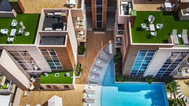 Vista aérea de un hotel moderno con varios pisos, una piscina central y zonas de estar al aire libre.
