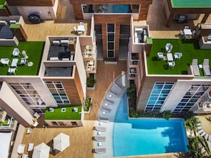 An aerial view of a modern hotel with multiple floors, a central swimming pool, and outdoor seating areas.