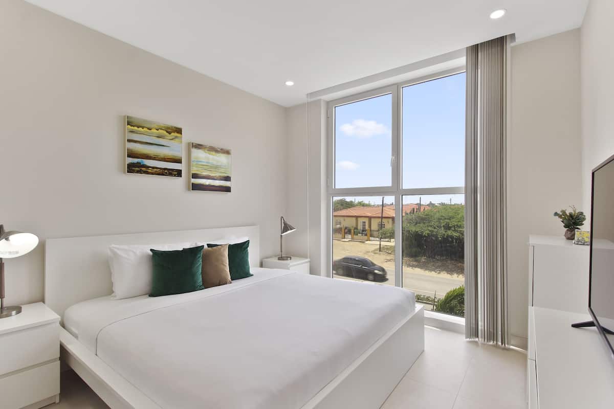 A modern hotel room with a large bed, a TV, and a window with a view of the outside.