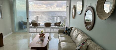 A modern living room with a leather sofa, a wooden coffee table, and a view of the ocean through large glass doors.