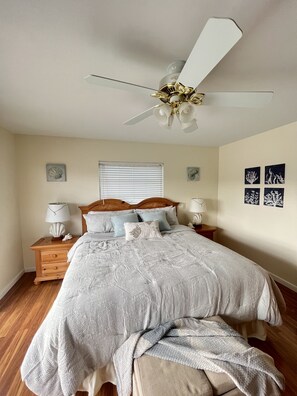 Un dormitorio con cama, mesitas de noche de madera, ventilador de techo y decoración en la pared.