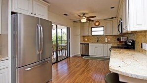 A kitchen with white cabinets, a stainless steel refrigerator, a ceiling fan, and a large window. - Dock Beach House in Sombrero Beach (Marathon)