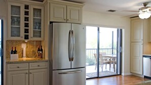 A kitchen with a stainless steel refrigerator, white cabinetry, and a sliding glass door leading to a balcony. - Dock Beach House in Sombrero Beach (Marathon)