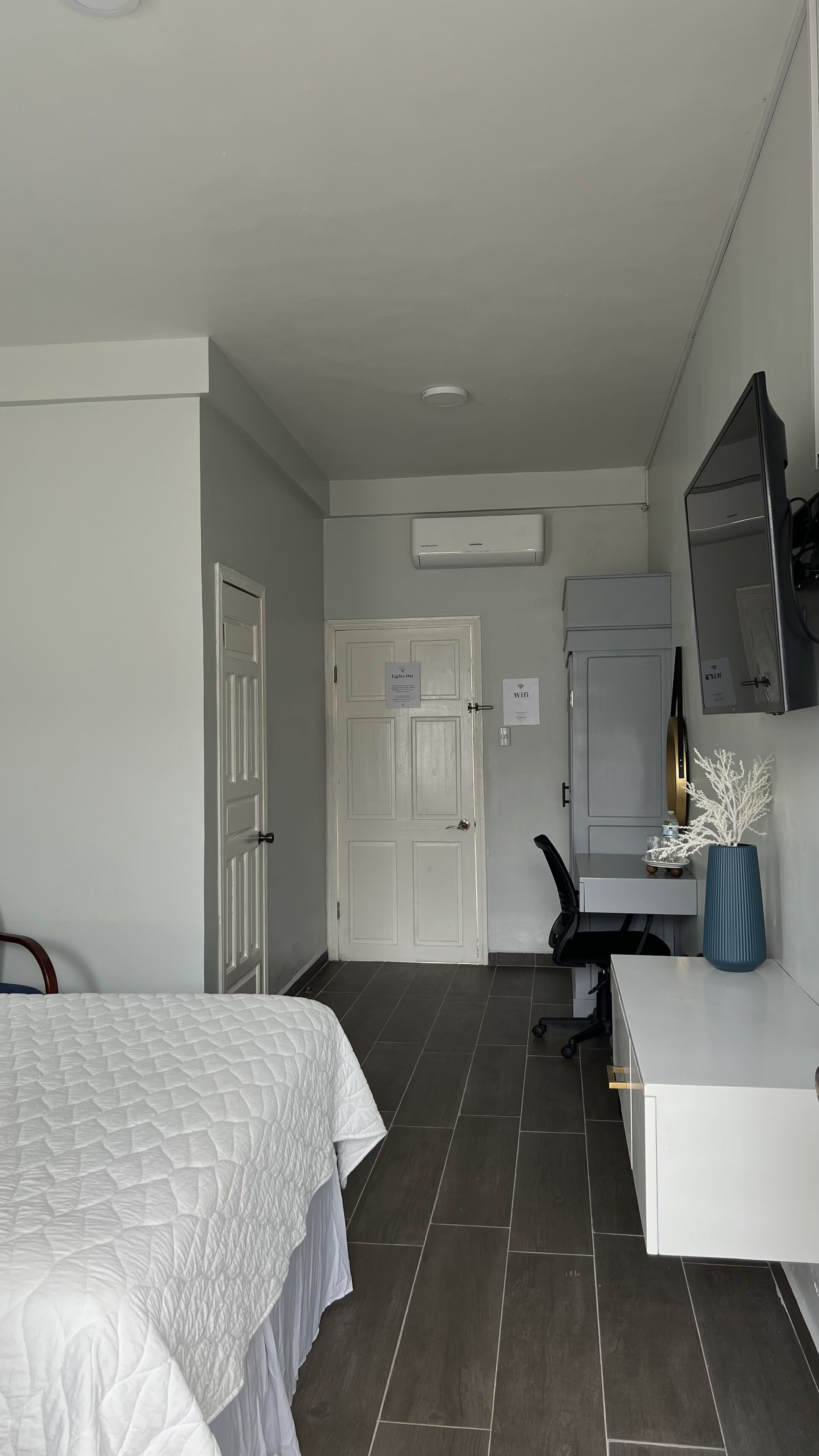 Ein Hotelzimmer mit einem Bett, einem Schreibtisch mit Computer, einem Stuhl, einem Spiegel und einer Tür.