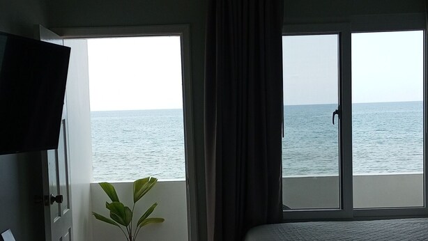 Un dormitorio con cama, televisor, planta en maceta y vista al mar a través de amplios ventanales.