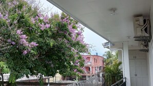 Un balcón cubierto con vistas a un edificio y un árbol con flores moradas.