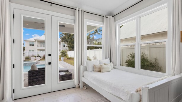 A bedroom with a large window, a bed, and a view of a swimming pool and neighboring houses. - Seagrove Beach - Private Pool + Spa - Bikes (Seagrove)