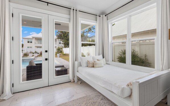Ein Schlafzimmer mit großem Fenster, einem Bett und Blick auf einen Pool sowie angrenzende Häuser.