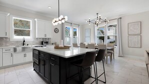 A modern kitchen with a large island, white cabinetry, and black bar stools. - Seagrove Beach - Private Pool + Spa - Bikes (Seagrove)