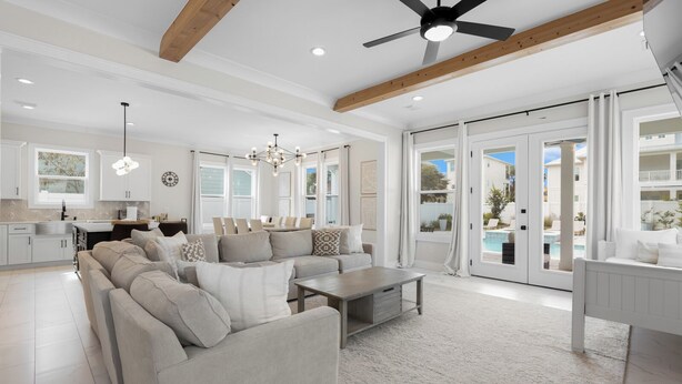 A spacious living room with a large sectional sofa, a coffee table, and a dining area with a white table and chairs. There is a kitchen area with white cabinets and a pendant light. The room has large windows and a view of a pool outside. - Seagrove Beach - Private Pool + Spa - Bikes (Seagrove)