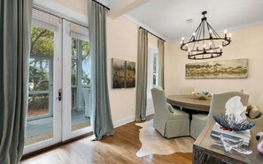 A dining area with a round table, chairs, a chandelier, and artwork on the walls. - Large Home + Private Pool, Beach & Steps to Beach (Seacrest)