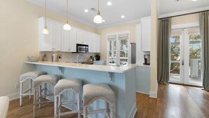 A kitchen with a central island, bar stools, white cabinets, and a view to the outside.