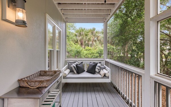 A covered porch with a white bench, a wicker basket, and a wall-mounted light fixture.