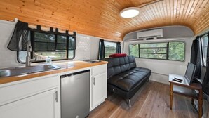Una cucina compatta con lavello, piano cottura ed elettrodomestici, un divano in pelle nera e un piccolo tavolo con un portatile.