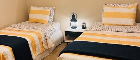 Ein Zimmer mit zwei Betten, jeweils mit gestreifter Bettwäsche, einem kleinen Tisch mit Lampe und einem gerahmten Bild an der Wand.