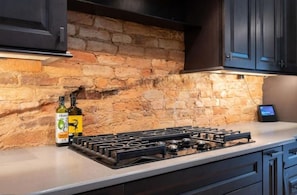 A kitchen with a gas stove, two bottles of olive oil, and a stone wall. - Luxury Loft Overlooking Downtown (Lincolnton)