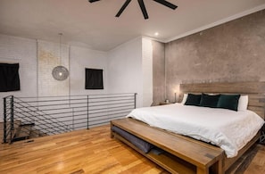 A modern bedroom with a wooden bed, a bench, a hanging light, and a metal railing. - Luxury Loft Overlooking Downtown (Lincolnton)