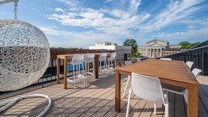 A rooftop terrace with a wooden table and white chairs, a spherical hanging chair, and a view of buildings in the background. - Luxury Loft Overlooking Downtown (Lincolnton)