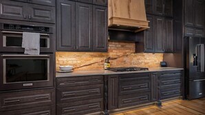 A modern kitchen with dark cabinetry, a brick backsplash, and stainless steel appliances. - Luxury Loft Overlooking Downtown (Lincolnton)